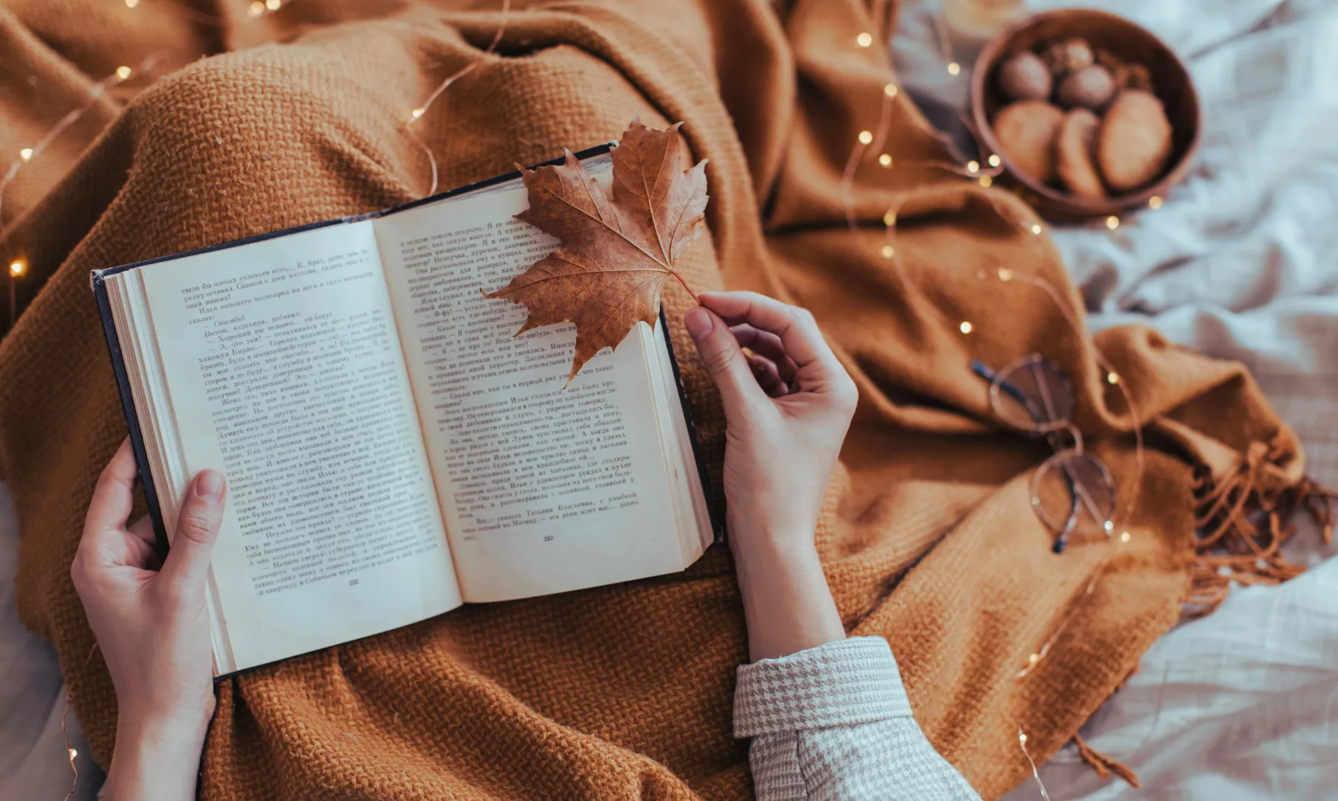 a girl holding book and a leaf with cookies and blanket in the background