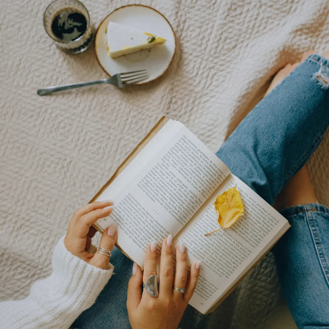 a girl reading a book with pastry and coffee in the background