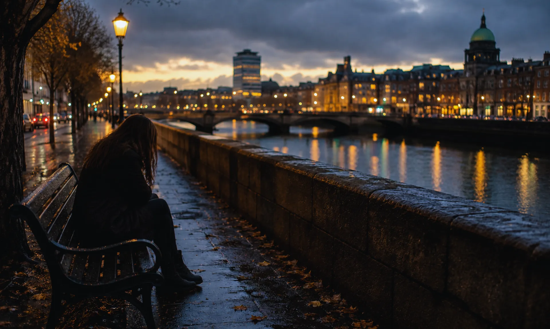 a-girl-sitting-alone-on-bench A solitary woman sits alone on a riverside bench at dusk, gazing across a rain-soaked cityscape as streetlights reflect on wet pavement, capturing themes of loneliness, longing, and emotional despair.